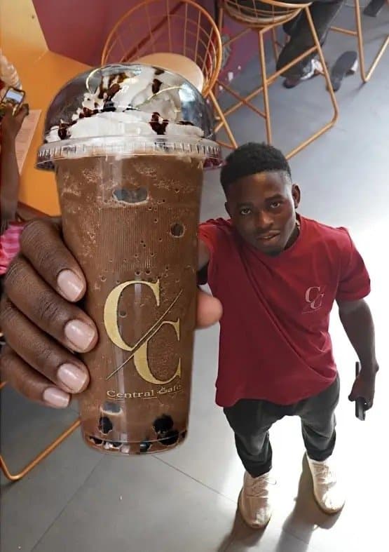 A chocolate boba shake topped with cream, held up in front of a customer in a red shirt