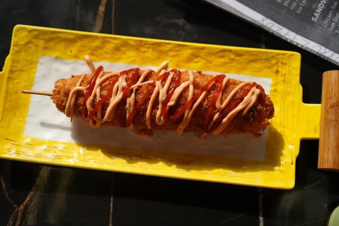 A Korean corn dog with sauce on a yellow board