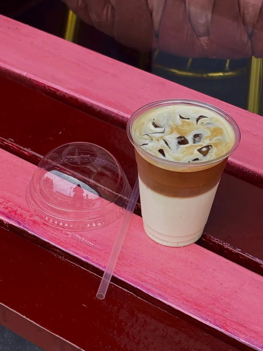 A layered iced latte on a pink bench