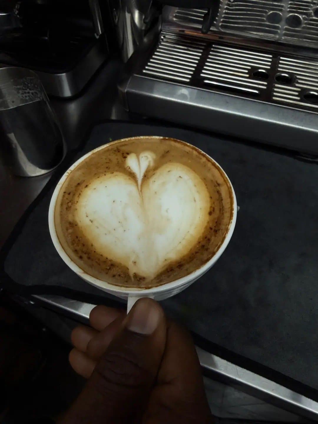 A heart poured into a latte, held over the espresso machine