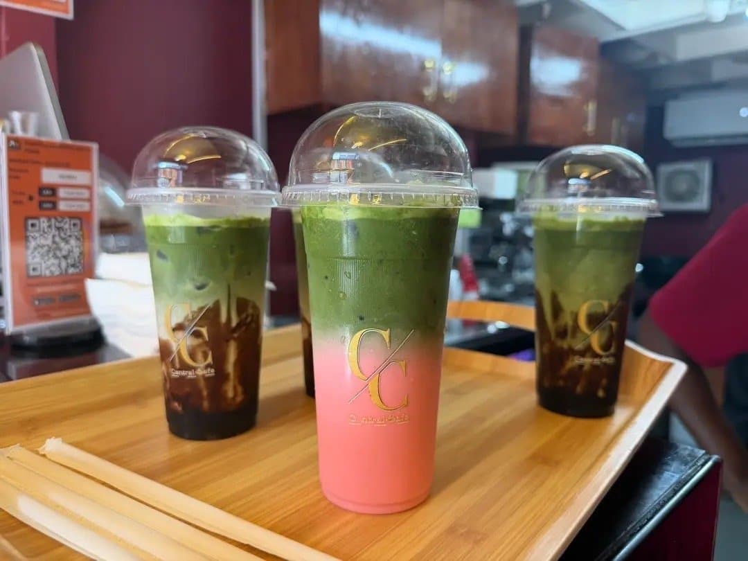 Three matcha drinks on a wooden tray, one with a pink layer