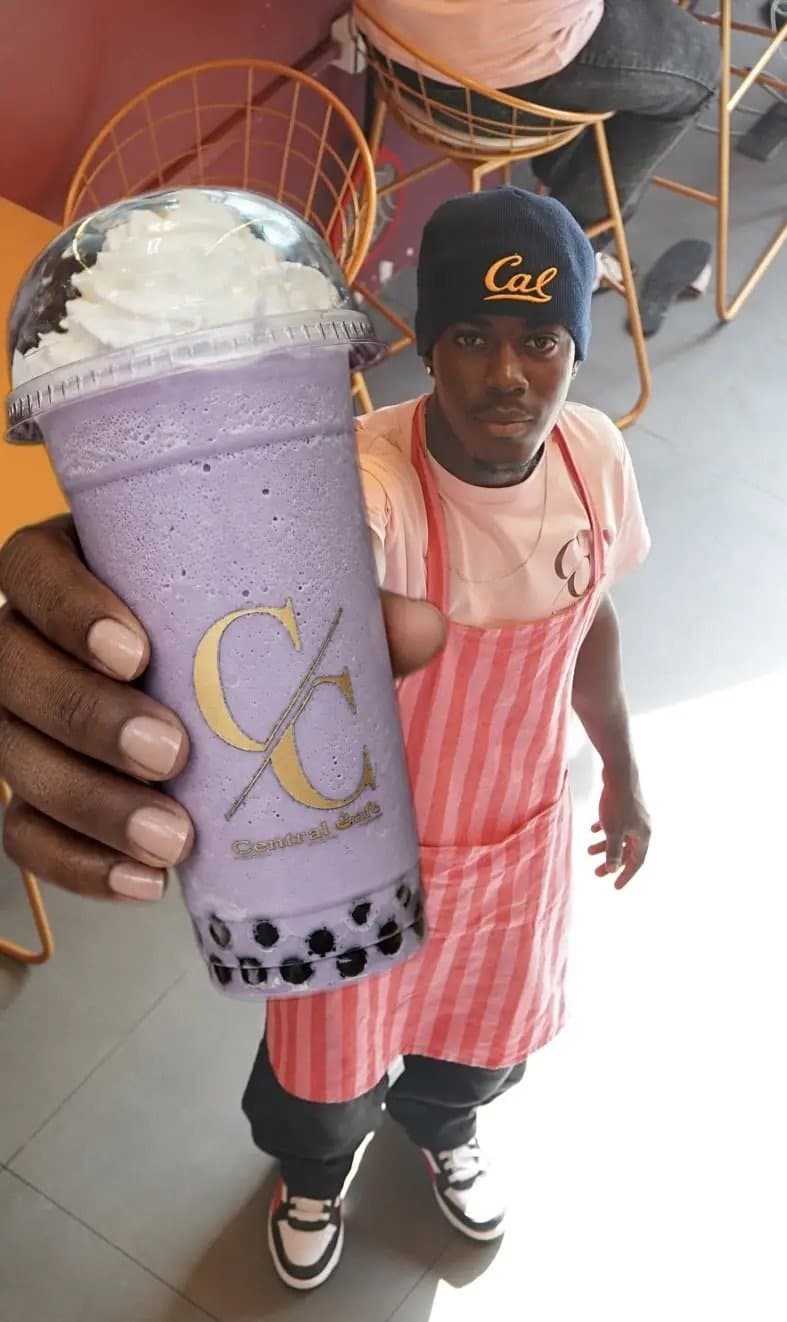 A taro boba held up beside a barista in a striped apron