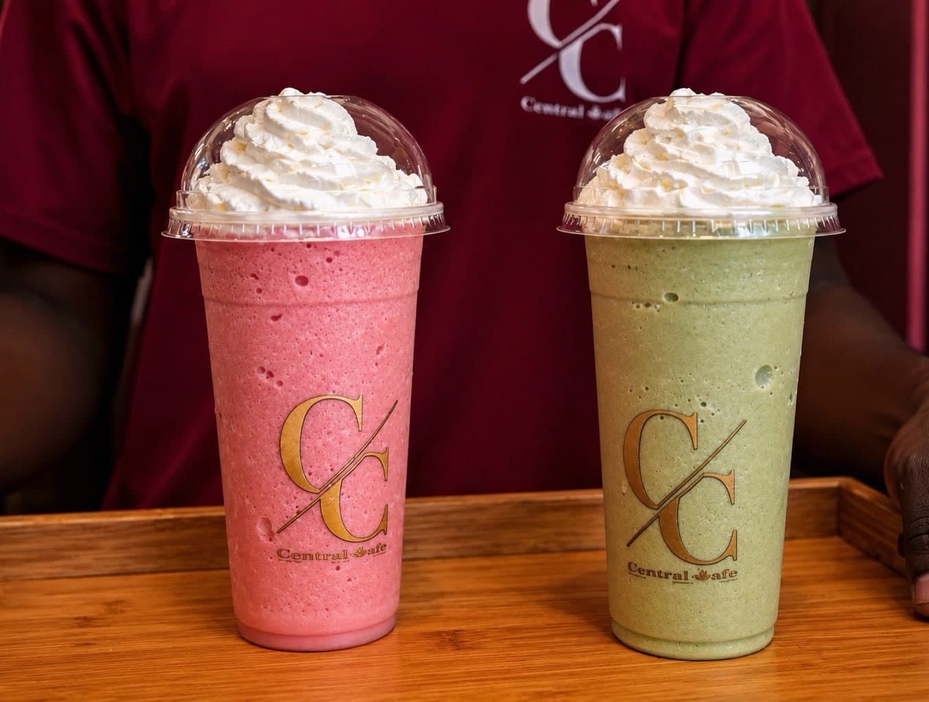 A strawberry frappé and a matcha frappé in Central Cafè cups on a wooden tray
