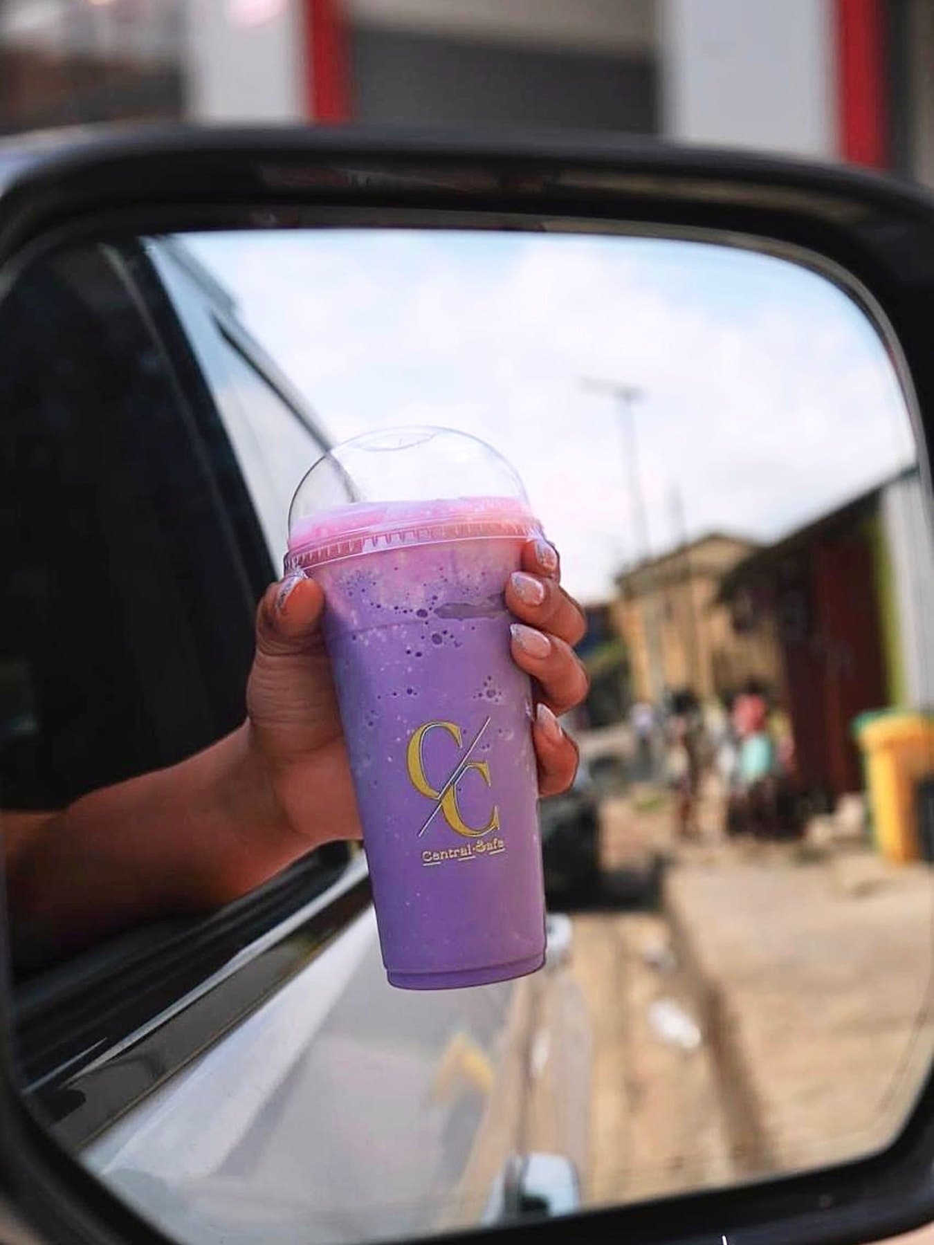 A taro shake in a Central Cafè cup held out of a car window, with a Monrovia street reflected in the wing mirror